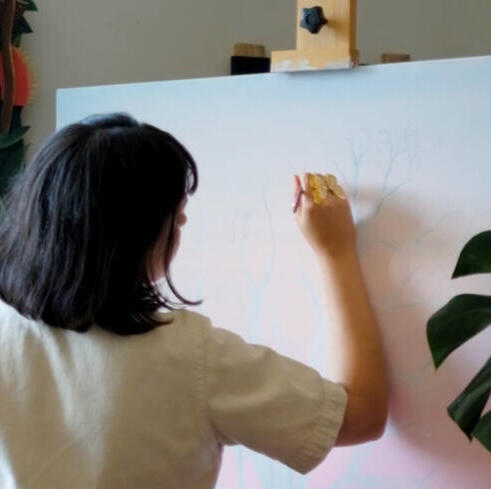 The back of a woman with short hair painting on a canvas.
