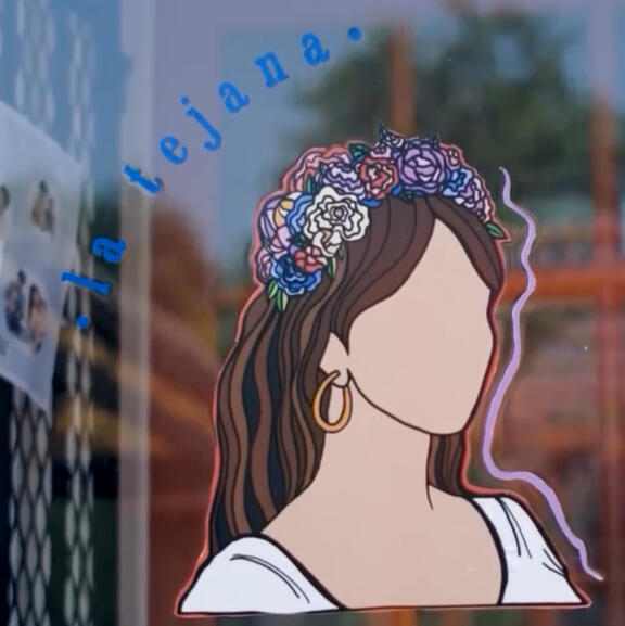 A storefront window with the image of a faceless female figure with flowers in her hair. Above it reads "la tejana"