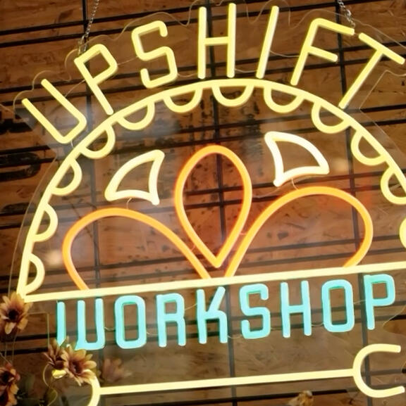 A neon store sign that reads "UPSHIFT WORKSHOP", featuring a wrench.